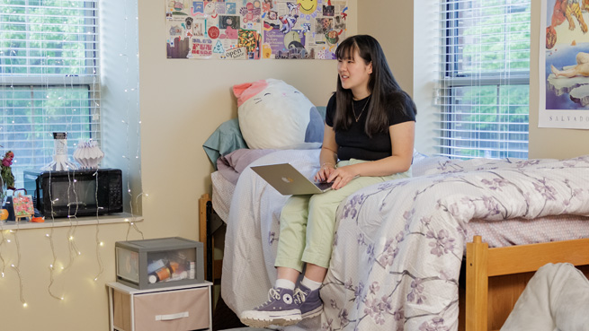 student sitting on dorm room bed with her laptop