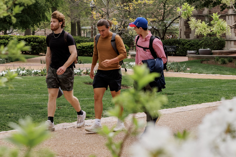 three students walking on campus with flowers in foreground