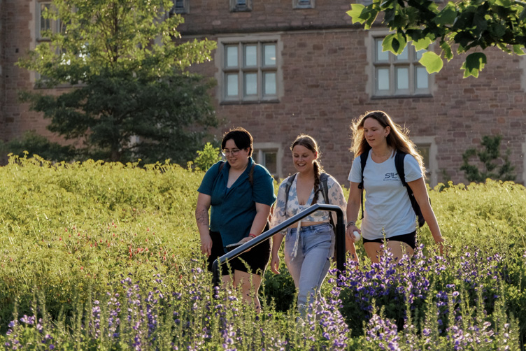 Students walk past spring flowers in front of Hillman Hall and Brown Hall